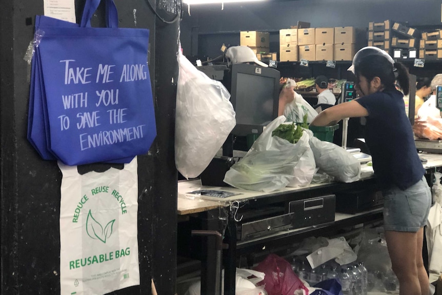 Blue reusable shopping bags hanging on the wall at a fruit and veg shop.