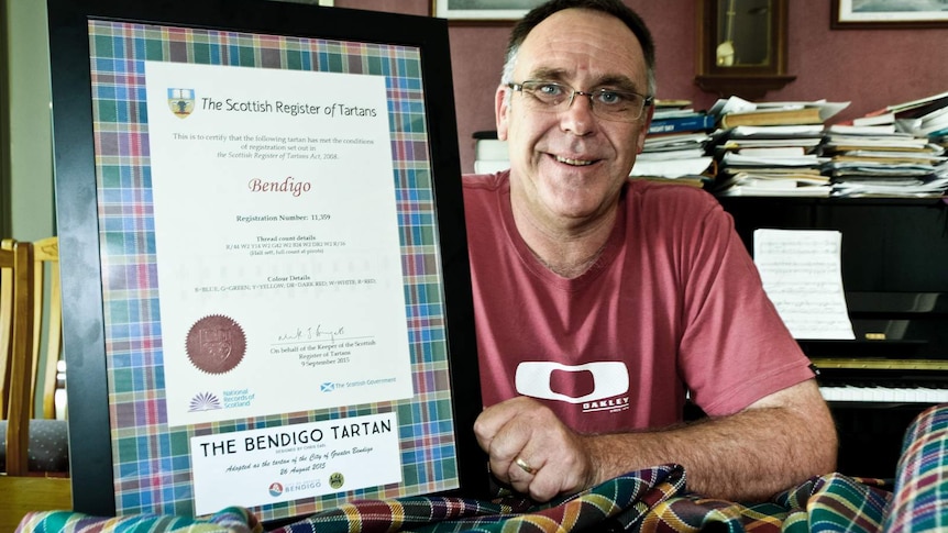 A man holding a framed certificate of the Scottish Register of Tartans