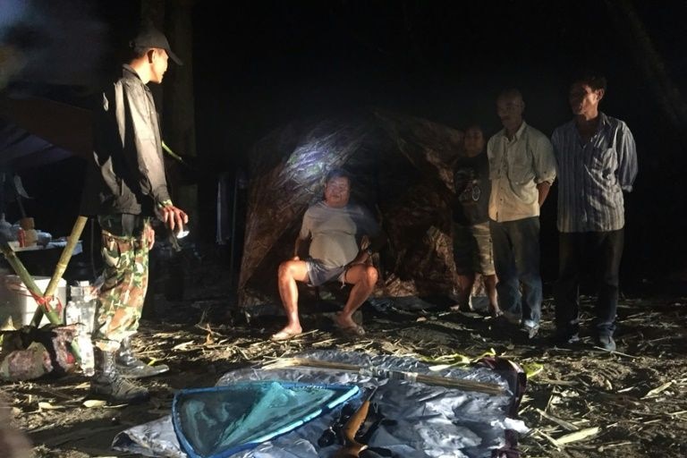 Mr Premchai sits outside his tents as rangers point to guns and hunting equipment found in raid