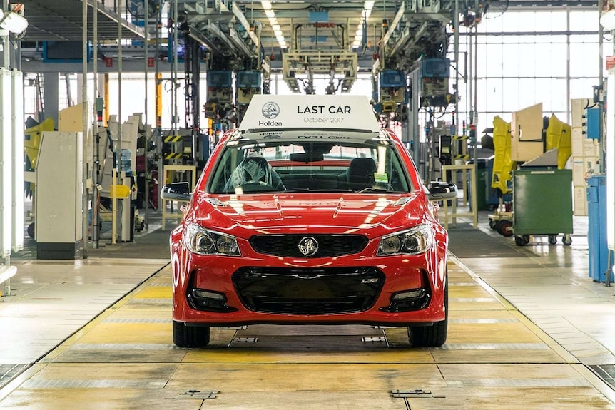 A red Holden Commodore sedan with a 'last car' sign affixed to its roof, on rolling off the Elizabeth Holden factory floor.