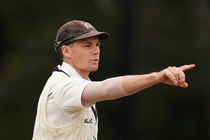 Peter Handscomb, wearing whites and his Victoria cap, points to something.