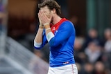 A Demons AFL player holds his face in his hands.