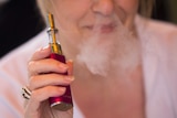 A woman holding an e-cigarette blows smoke through her nostrils.