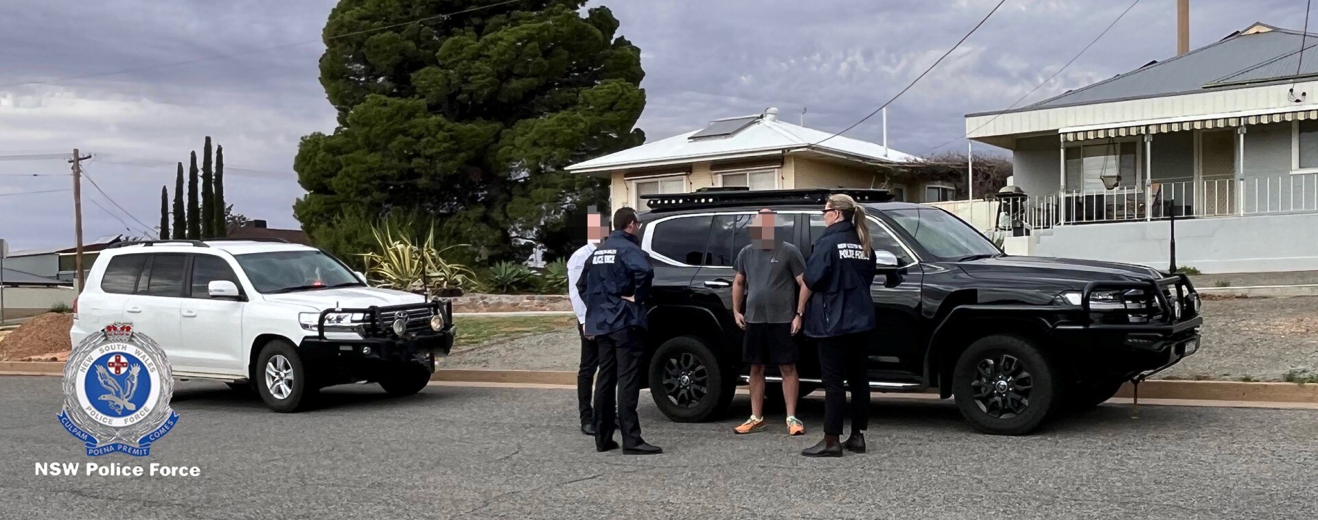 Two police officers standing on a road in front of a vehicle with two men with their faces blurred.