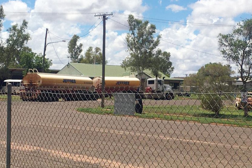 A photo of a water truck, taken through a fence.