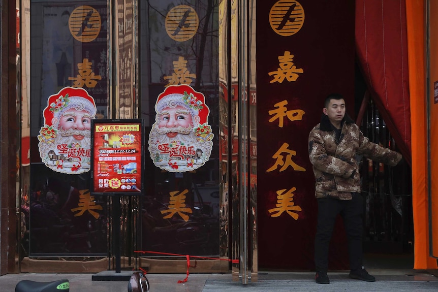 A worker guards the entrance of a shop decorated with images of Santa Claus.