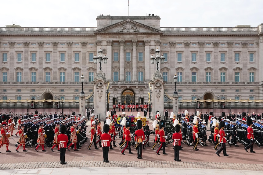 A procession with a coffin passes Buckingham Palace.