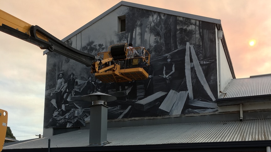 A man on a forklift with a painting on the wall of the building behind him