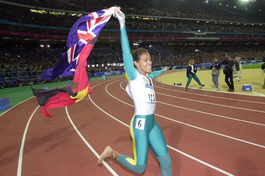 Cathy Freeman smiles and runs on track holding flags after Sydney 2000 Olympic win.