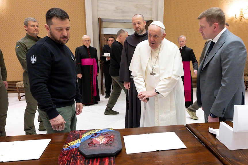 Volodymyr Zelenskyy (L) and the pope look at a bulletproof vest painted by a Ukrainian solidier with the Madonna on it.