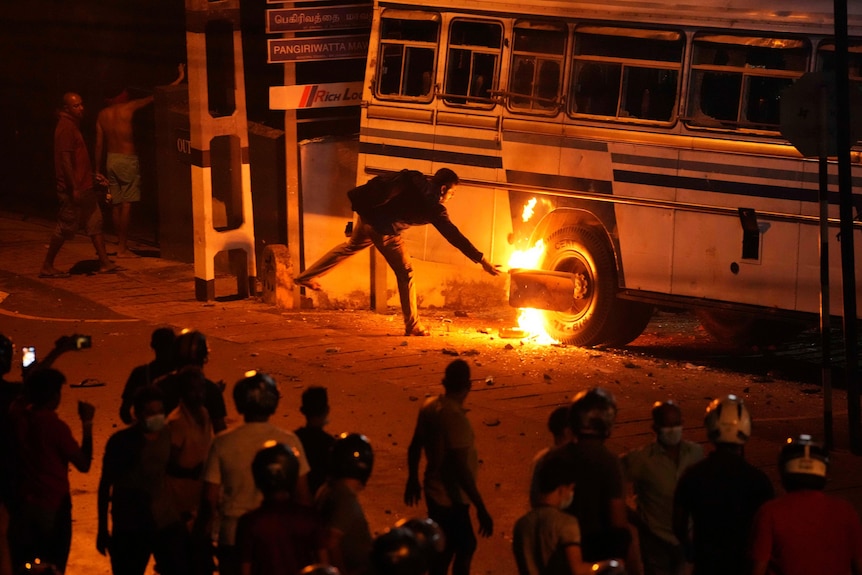 A protester tries to burn a bus outside Sri Lankan president's private residence as a group of riot police approach.