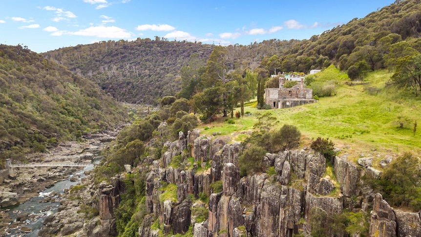 A wide shot of the Launceston Gorge and suspension bridge with historic stone building on a cliff top