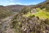 A wide shot of the Launceston Gorge and suspension bridge with historic stone building on a cliff top