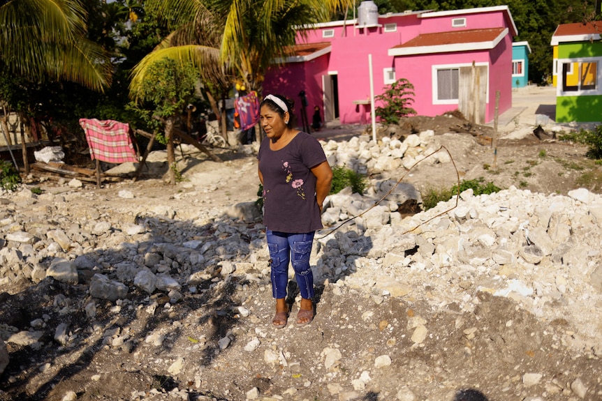 A woman stands on rubble as brightly coloured homes are seen in the background. 