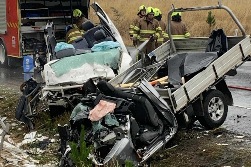 Two wrecked vehicles on the side of a country road. A fire truck and firefighters are in the background