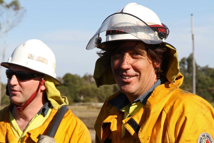 Two firefighters in full gear look toward camera.