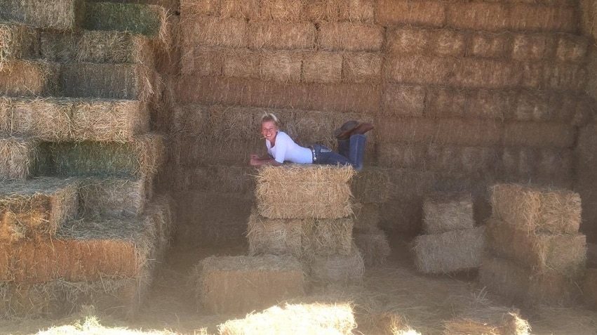 Ruth Hole lying on a hay bale in front of a big stack of bales in their shed at Ulan, NSW.