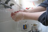 Soapy hands being washed under a running tap.