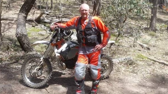 A man wearing orange and black stands next to a trail bike.