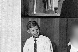 A black-and-white photo smiling boy in a white shirt and tie sitting at a breakfast table at a school.