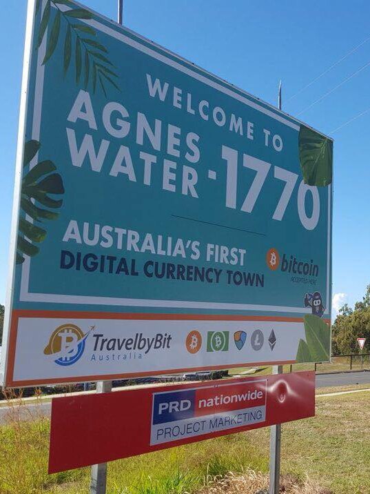 A billboard on a street corner reads 'Welcome to Agnes Water-1770 Australia's first digital currency town'