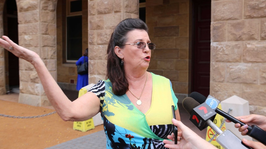 Margaret Dodd with her hand thrown out, in front of microphones.