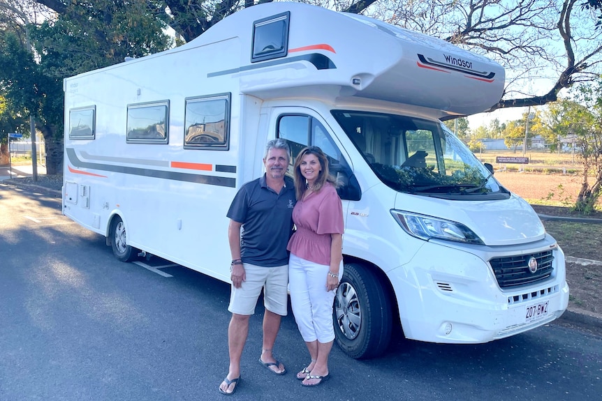 A couple is standing in front of a modern large white camper van