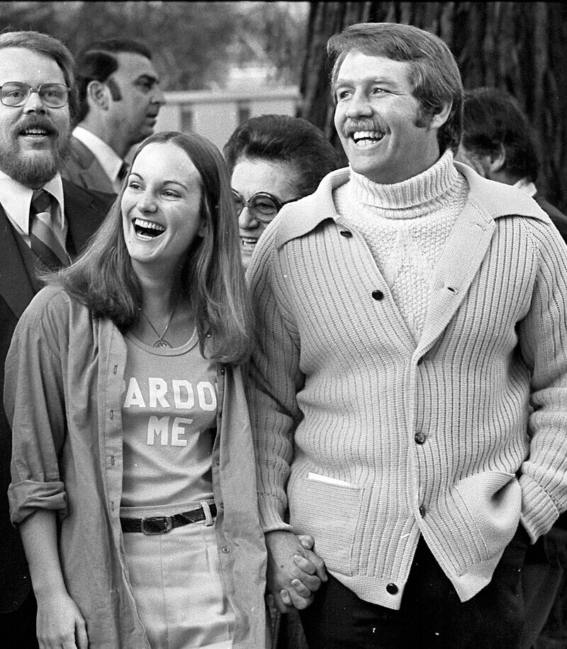 A woman holds hands with a tall moustachioed man