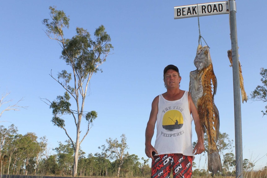 Clayton Offord stands beside dead fish dangling from a road sign