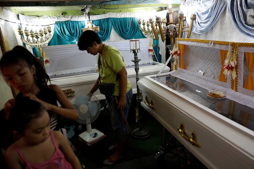 Relatives inside a room where two caskets with bodies are located.