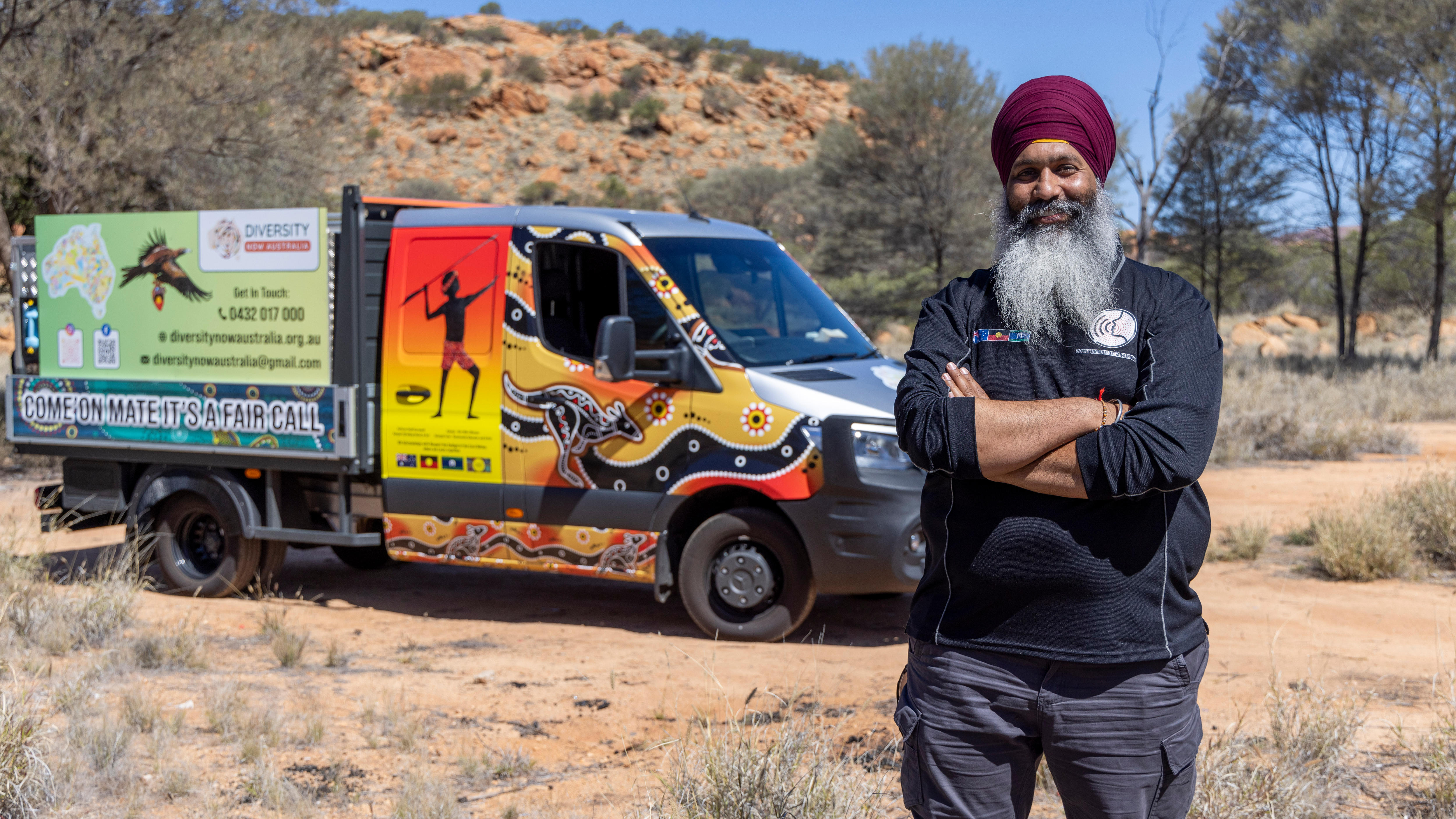 A man in a turban stands in front of a van covered in Indigenous artwork. 