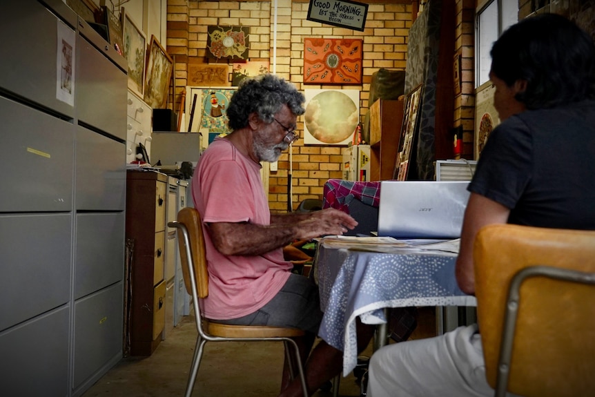 Donald Craigie sits at a desk in his home. Posters and filing cabinets adorn the walls.