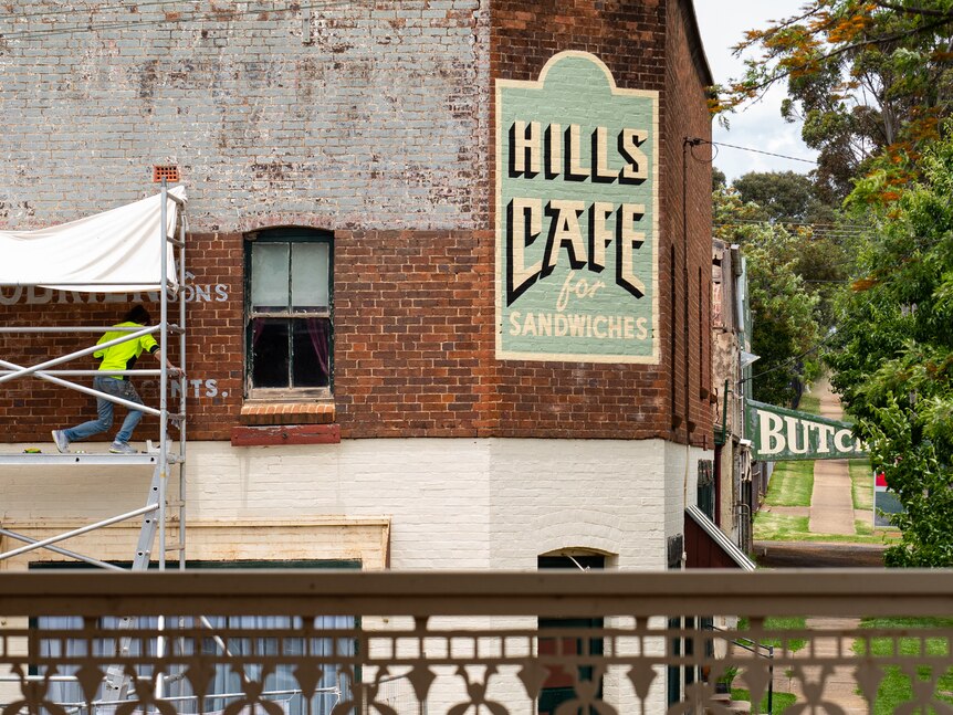 A wide shot of a woman on scaffolding painting a wall.