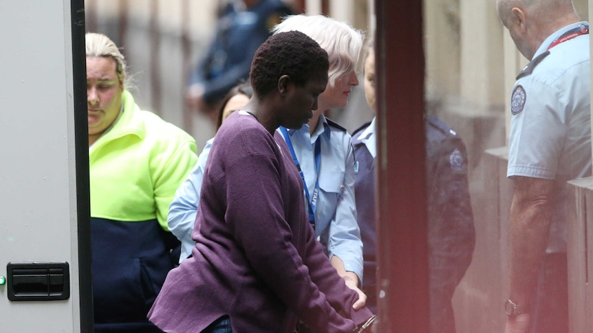 Akon Guode, in handcuffs, being escorted by a police officer from a prison van.