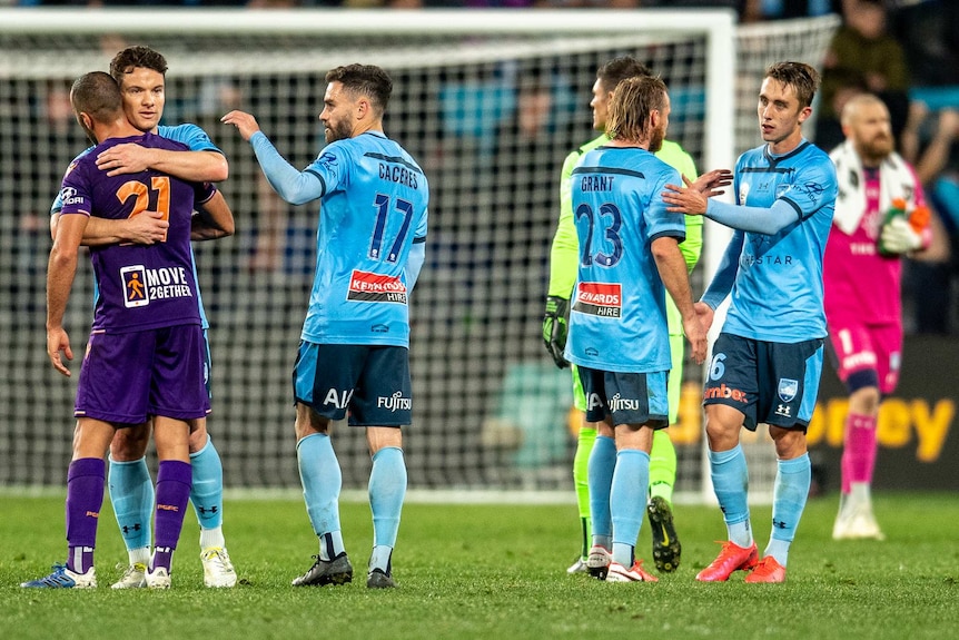 A Sydney FC A-League player hugs a Perth Glory opponent, as three of his teammates walk nearby.