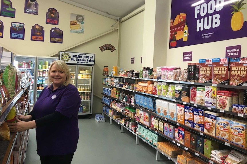 Lynne Neshoda standing between shelves stacked with food, including cereal and long-life milk.