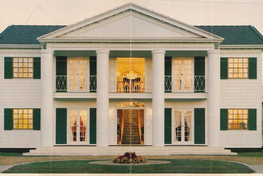 A two-story, white home with four large pillars framing a grand front entrance and staircase. 