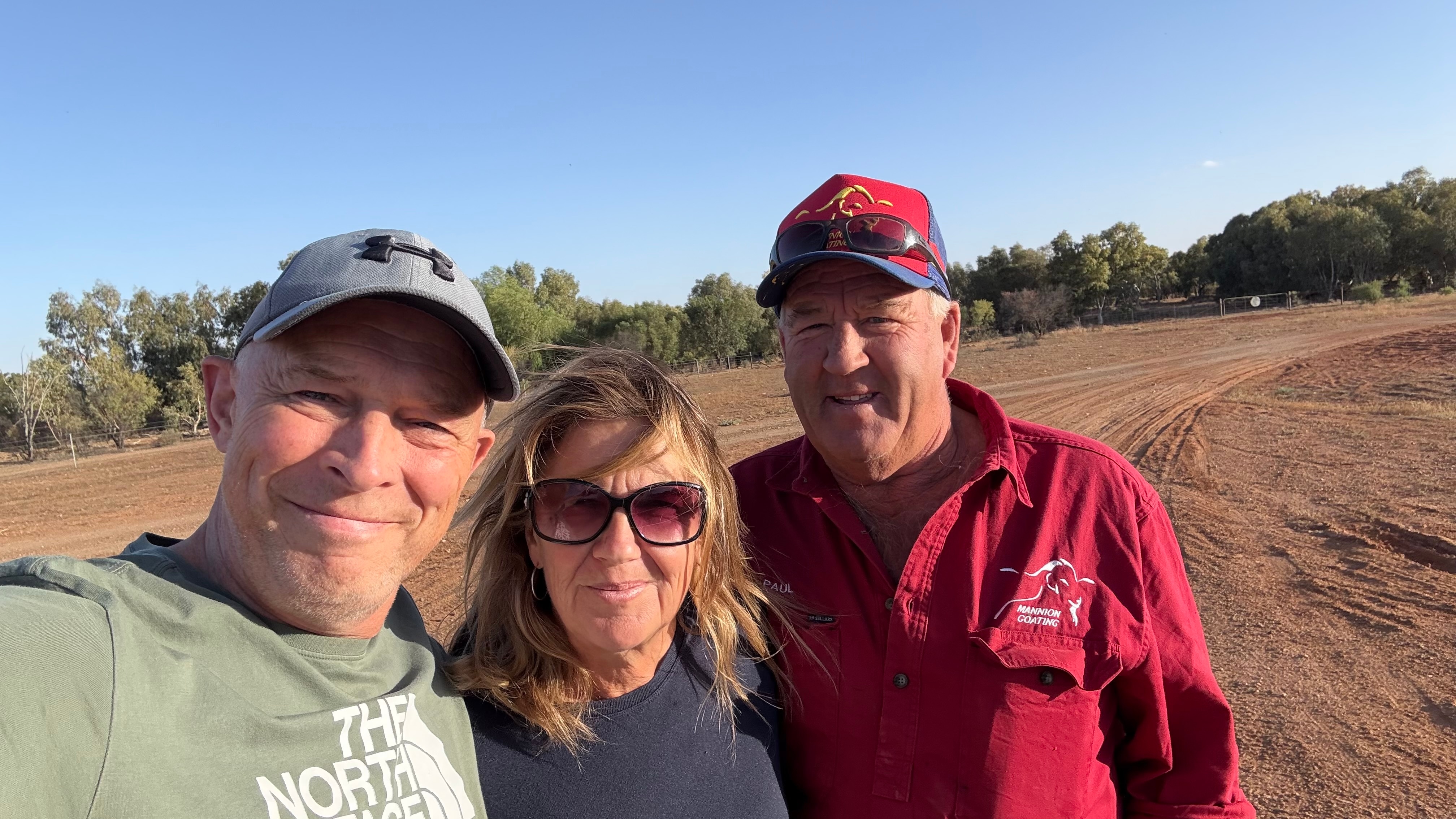 um homem de cinza com camisa verde abraça uma mulher de óculos e camisa azul ao lado do homem de camisa vermelha.