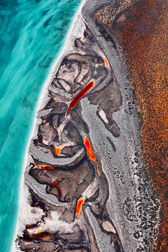 Aerial image of a blue shoreline with grey and red coloured landscape.