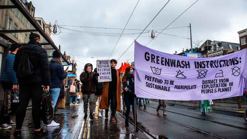 A group of protestors on a wet, rainy day in Amsterdam in 2021. People hold a banner on greenwashing