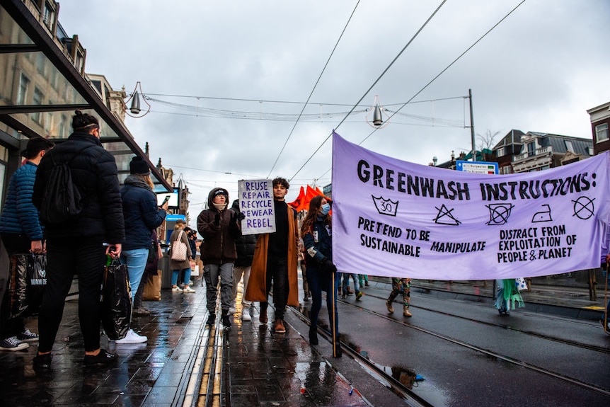 Climate activists protest on a wet, rainy day in Amsterdam in 2021. People hold a banner on greenwashing