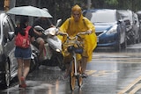 A person in a yellow raincoat rides a bike down a city street in the rain. 