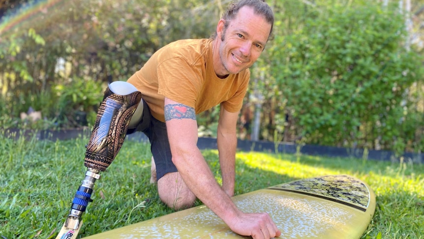 Man with prosthetic leg waxing a surfboard in the backyard, smiling