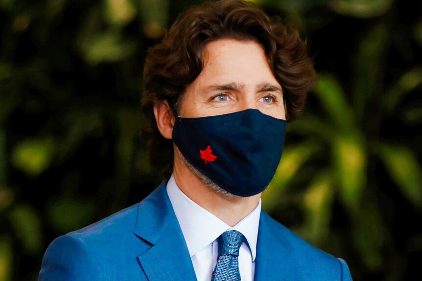 Justin Trudeau in a blue suit and black masking bearing the Canadian maple leaf