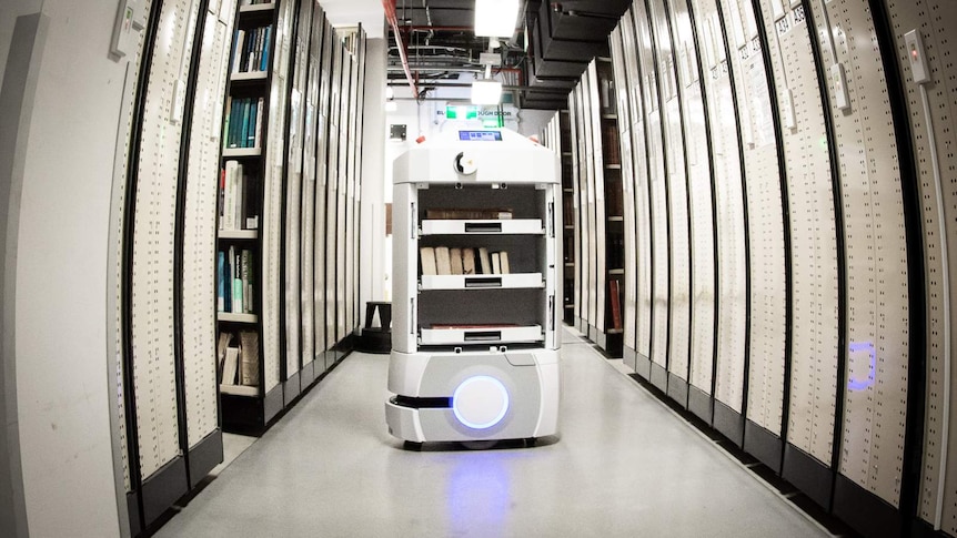 An Automated Guided Vehicle is travelling down a large stack of books.