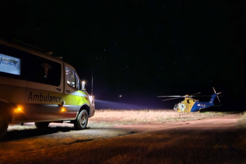 A helicopter parked next to an ambulance at night