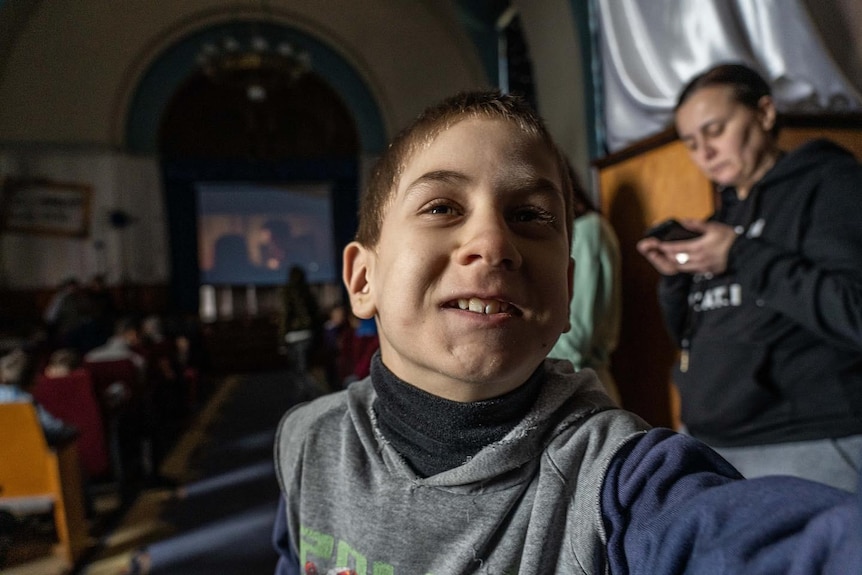 A boy with brown hair and wearing a grey jumper smiles into the camera.