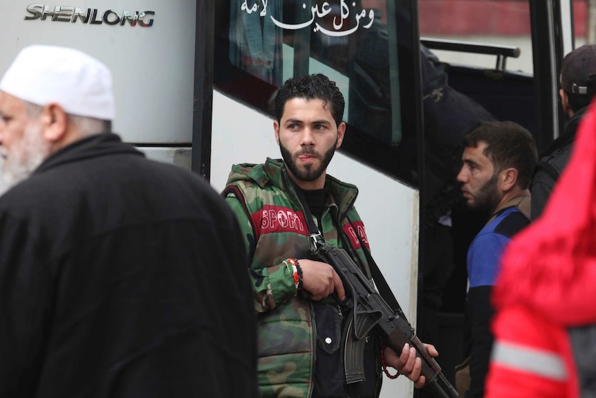 An militant shouldering an automatic rifle prepares to board a bus.