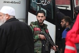 An militant shouldering an automatic rifle prepares to board a bus.