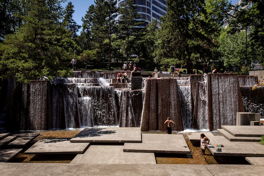 People standing in a large man-made waterfall in a public park. 